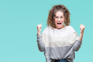 Güzel esmer kıvırcık saçlı Genç kız izole arka plan üzerinde kutluyor gözlük takan şaşırttı ve silah ile başarı için hayran kaldırdı ve gözleri açık. Kazanan kavramı.