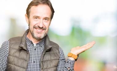 Orta yaş yakışıklı adam neşeli sunulması ve kameraya bakarak avucunun ile işaret gülümseyen kış yelek giyiyor.