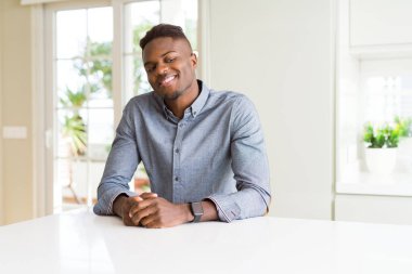 Beyaz masa uzak tarafına gülümseme ile yüzünde, doğal ifade görünümlü yakışıklı adam Afro-Amerikan. Kendine güvenen gülüyor.