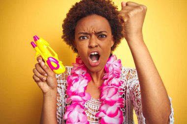 Afro saç giyen çiçek Hawaiian Lei ve su tabancası ile genç Afrikalı Amerikalı kadın rahatsız ve öfke, deli ve yükseltilmiş el, öfke kavramı ile bağırarak bağırıyor sinirli