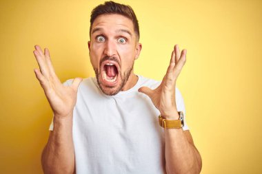 Sarı izole arka plan üzerinde rahat beyaz t-shirt giyen genç yakışıklı adam deli kutluyor ve başarı için hayran silah kaldırdı ve açık gözleri heyecanlı çığlık. Kazanan kavramı