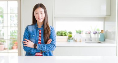 Beyaz masada kot ceket giyen güzel Asyalı kadın yüzünde ciddi ifade ile rahat. Çapraz kollarla basit ve doğal