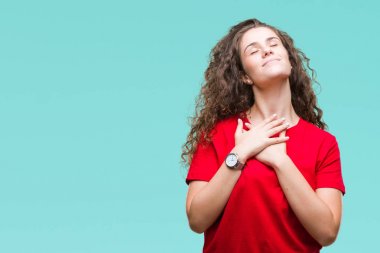 Güzel esmer kıvırcık saçlı Genç kız rahat giyiyor bakın arka plan ile kapalı gözler göğüs ellerinde ve yüzünde minnettar jest ile gülümseyen izole. Sağlık kavramı.