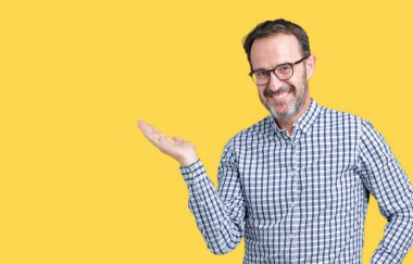 Neşeli sunulması ve kameraya bakarak avucunun ile işaret gülümseyen izole arka plan üzerinde gözlük takan yakışıklı orta yaş zarif üst düzey iş adamı.