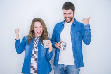 Genç güzel çift beyaz izole arka plan üzerinde bir fincan kahve içme gurur çığlık ve zafer ve başarı çok heyecanlı kutluyor, duygu tezahürat