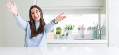 Sarılmak için Kollarını açarak gülümseyen kamera geniş açı resim güzel genç kadının evde beyaz masaya oturan bakarak. Neşeli ifade kucaklayan mutluluk.