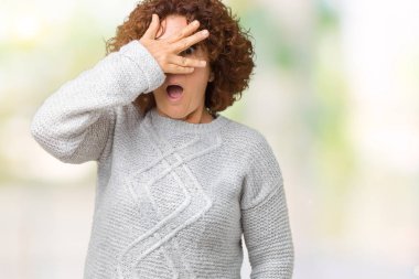 Mahcup ifadeyle parmaklarımın arasından seyir yüz ve gözler el ile kapsayan şok bakmak izole arka plan üzerinde kış kazak giyen güzel orta ager üst düzey kadın.