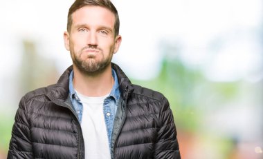 Yakışıklı adam komik surat ile yanakları şişirme kış palto giyiyor. Ağız ile hava, deli ifade şişirilmiş.