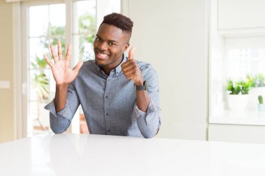 Yakışıklı afro-amerikan adam beyaz masada gösteren ve parmakları ile işaret ederken altı numara kendinden emin ve mutlu gülümseyerek.