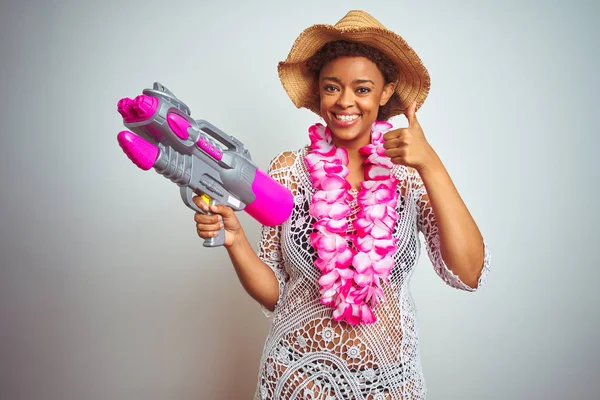 Young african american woman with afro hair wearing flower hawaiian lei and water gun happy with big smile doing ok sign, thumb up with fingers, excellent sign