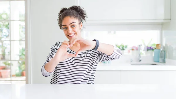 Beautiful african american woman with afro hair wearing casual striped sweater smiling in love doing heart symbol shape with hands. Romantic concept.