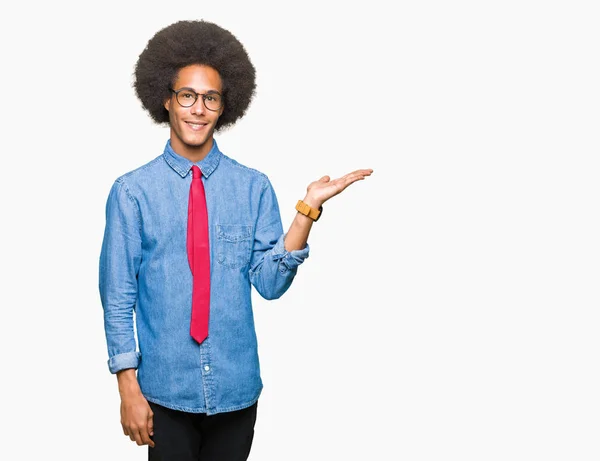 年轻的非洲裔美国商人戴着非洲头发戴着眼镜 戴着红色领带 微笑着愉快地呈现 用手掌指着手掌看着镜头 — 图库照片