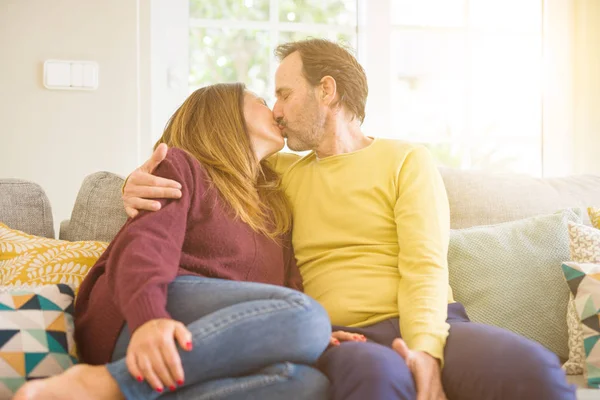 ソファに座って自宅でキスをする中年のロマンチックなカップル — ストック写真