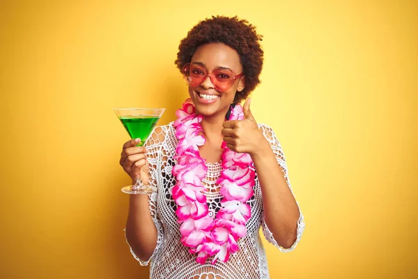 Young african american woman with afro hair wearing flower hawaiian lei and drinking a cocktail happy with big smile doing ok sign, thumb up with fingers, excellent sign