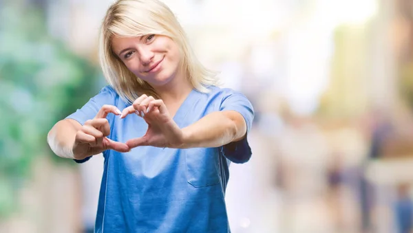 美しい金髪の若い看護師医師女性のハートマークと手で形を示す愛の笑みを浮かべて孤立の背景の上 ロマンチックな概念 — ストック写真