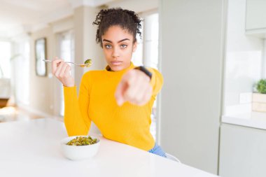 Afro-Amerikalı sağlıklı sebzeler yiyen genç bir kadın kamerayı işaret ediyor ve sen, el işareti, ön taraftan pozitif ve kendinden emin bir jest.