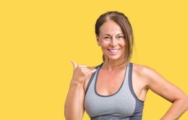 Güzel orta yaş kadın spor kıyafetlerle yapıyor gülümseyen izole arka plan üzerinde telefon hareketi ile el ve parmak telefonda konuşuyor gibi. Kavramları iletişim.