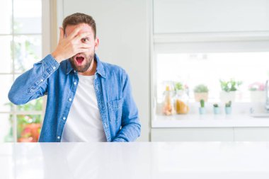 Yakışıklı adam evde şok yüz ve gözleri el ile kapsayan gözetleme, utanmış ifade ile parmaklarından bakarak.