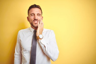 Genç yakışıklı iş adamı diş ağrısı veya diş üzerinde diş hastalığı nedeniyle ağrılı ifade ile el ile el ile ağız dokunmadan sarı izole arka plan üzerinde zarif beyaz gömlek giyiyor. Diş hekimi konsepti.