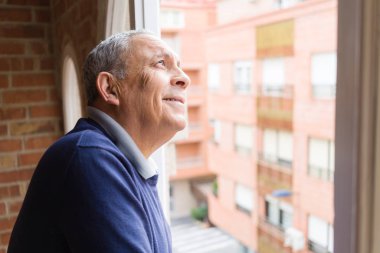 Gelecek için bakan pencerenin yanında, neşeli, mutlu ve olumlu gülümseyen yakışıklı orta yaş üst düzey adam