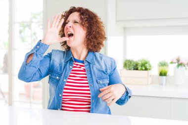 Evde kot ceket giyen kıvırcık saçlı orta yaş yaşlı kadın bağırarak ve ağızda el ile yan yüksek sesle bağırıyor. İletişim kavramı.