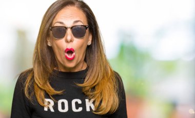 Güneş gözlüğü ve rock'n roll kazak korkuyor ve şok sürpriz ifade, korku ve heyecan yüz ile giyen güzel orta yaş kadın.