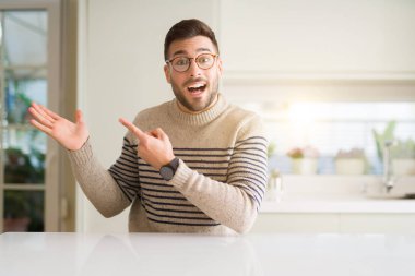 Evde gözlük takan genç yakışıklı adam hayran ve parmak ile işaret, elle sunulurken kameraya gülümsüyor.
