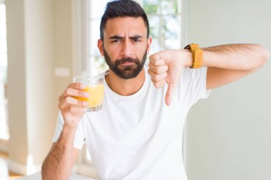 Yakışıklı İspanyol adam kızgın yüz ile sağlıklı portakal suyu içme, başparmak aşağı, ret kavramı ile sevmediğim gösteren negatif işareti