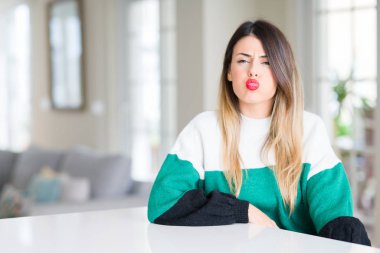 Evde kış kazak giyen genç güzel kadın komik surat ile yanakları şişirme. Ağız ile hava, deli ifade şişirilmiş.