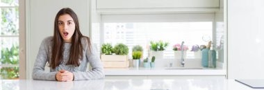 Güzel genç kadın evde korkuyor ve şok sürpriz ifade, korku ve heyecan yüz beyaz masada oturan geniş açı resim.