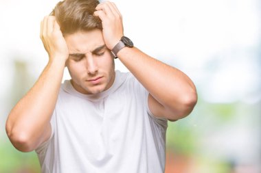 Genç yakışıklı adam beyaz t-shirt giyiyor çünkü umutsuz ve stresli baş ağrısı acı izole arka plan üzerinde ağrı ve migren. Ellerini kafasına.