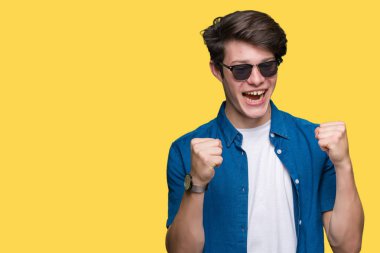 Yakışıklı delikanlı izole arka plan kutlama üzerinde güneş gözlüğü takıyor şaşırttı ve başarı için kaldırdı kollarını açarak hayret ve gözleri açık. Kazanan kavramı.