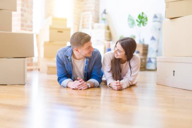 Evde karton kutular etrafında yerde yatan rahatlatıcı genç güzel çift, yeni bir eve hareket mutlu gülümseyen