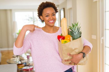 Kağıt torba sürpriz yüz işaret parmağı ile taze yiyecek tam kendisine tutan genç Afro-Amerikan kadın