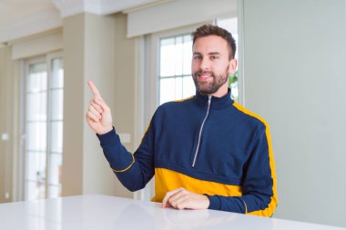 Kameraya bakarak yan el ve parmak ile işaret eden yakışıklı adam evde yüzünde kocaman bir gülümseme ile.