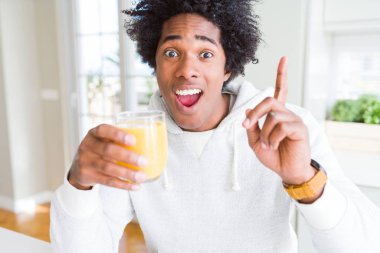 Afro-Amerikan adam tutan ve portakal suyu bardak içme mutlu yüz, bir numaralı ile bir fikir ya da soru işaret parmağı ile şaşırttı