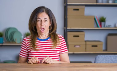 Orta yaş yaşlı kadın evde masada oturan şok karşısında, şüpheci ve alaycı görünümlü, açık ağız ile şaşırttı
