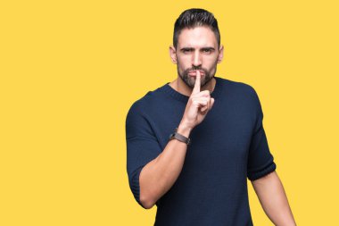 Dudaklarında parmak ile sessiz olmanı izole arka plan üzerinde kazak giyen genç yakışıklı adam. Sessizlik ve gizli kavramı.