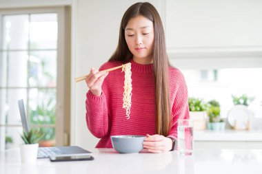 Güzel Asyalı kadın dizüstü bilgisayar kullanarak çalışan ve akıllı yüz ciddi düşünme emin bir ifade ile asya erişte yeme