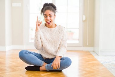 Afro saçlı güzel genç Afrikalı Amerikalı kadın yerde oturan başarılı bir fikir ile parmak yukarı işaret. Çıkıldı ve mutlu. Bir numara.