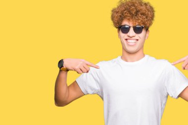 Yüzünde gülümseme ile kendinden emin görünüyorsun, kendini gururlu ve mutlu parmakları ile işaret güneş gözlüğü takıyor afro saçlı Genç yakışıklı adam.