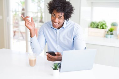 Akıllı telefon ve dizüstü bilgisayar kullanarak Afro-Amerikan iş adamı çok mutlu yan el ve parmak ile işaret