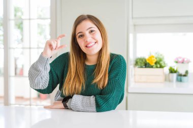 Genç güzel artı boyutu kadın rahat çizgili kazak giyen gülümseyen ve el parmakları görünümlü ve kamera ile küçük boyutlu işareti yapıyor kendinden emin gesturing. Ölçü kavramı.