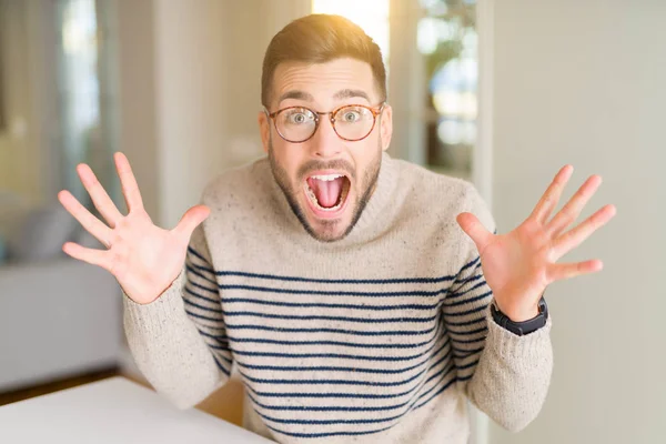 Evde gözlük giyen genç yakışıklı adam çılgın kutluyor ve başarı için hayran silah kaldırdı ve açık gözleri heyecanlı çığlık. Kazanan kavramı