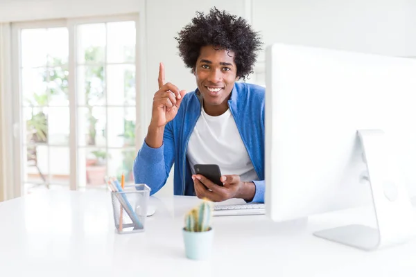 African American man working using smartphone and computer surprised with an idea or question pointing finger with happy face, number one