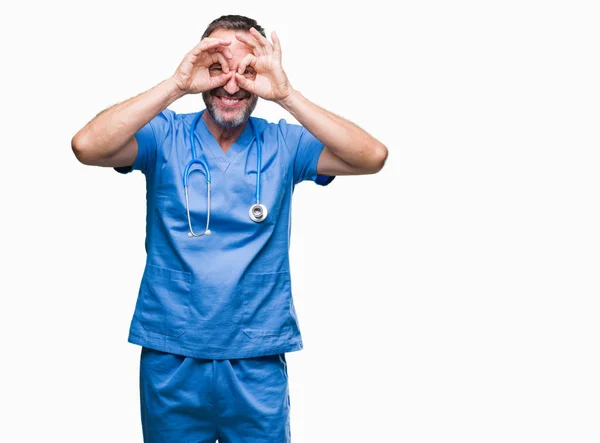 中年白发高级医生在孤立的背景下穿着医疗制服做确定的手势 就像双筒望远镜伸出舌头 眼睛透过手指看 疯狂的表达 — 图库照片
