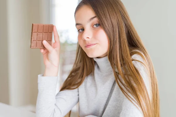 真剣に考えるスマートな顔に自信のある表情でチョコレートバーを食べる美しい若い女の子 — ストック写真