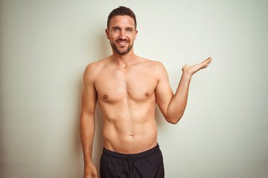 Izole arka plan üzerinde Genç yakışıklı gömleksiz adam neşeli sunan gülümseyerek ve kameraya bakarak avuç içi ile işaret.