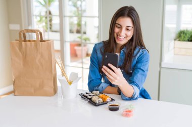 Güzel genç kadın ayakta ve emin bir gülümseme ile diş gösteren gülümseyen mutlu bir yüz ile akıllı telefon kullanarak uygulamadan gıda teslim sipariş