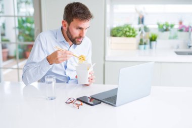 İş adamı yemek götürün Asya erişte yemek çalışma kullanırken bilgisayar dizüstü ve gülümseyen